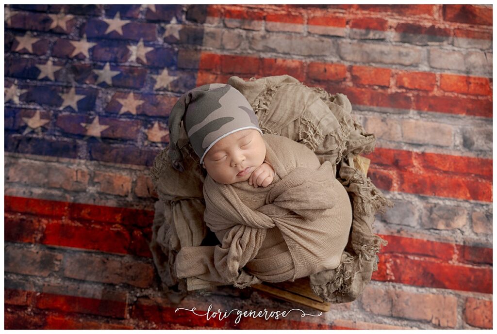 Newborn boy portrait photographed by Lori Generose of LG Photography, a Lehigh Valley newborn photographer, featuring a sleeping baby wrapped in neutral tones with an American flag backdrop during an in-studio session in Coplay, Pennsylvania.