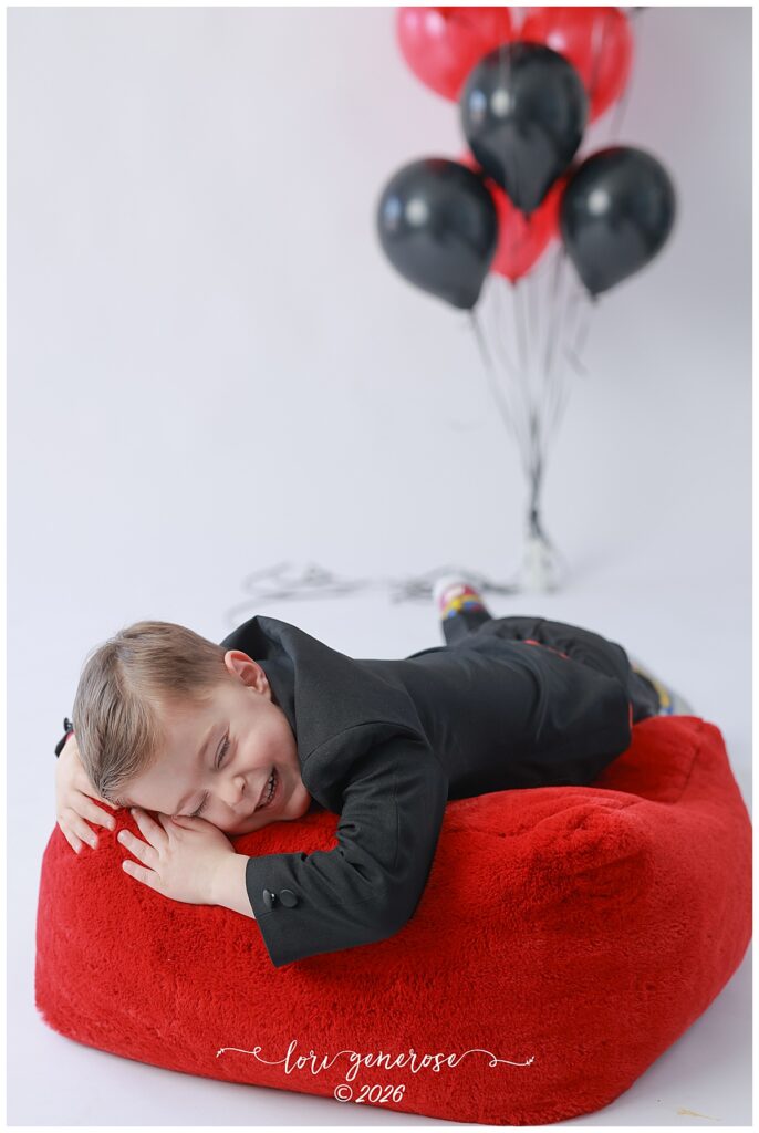 Valentine's Day photo by Lehigh Valley Photographer Lori Generose of LG Photography of an adorable little boy in a suit laying on/hugging a red plushy bean bag chair