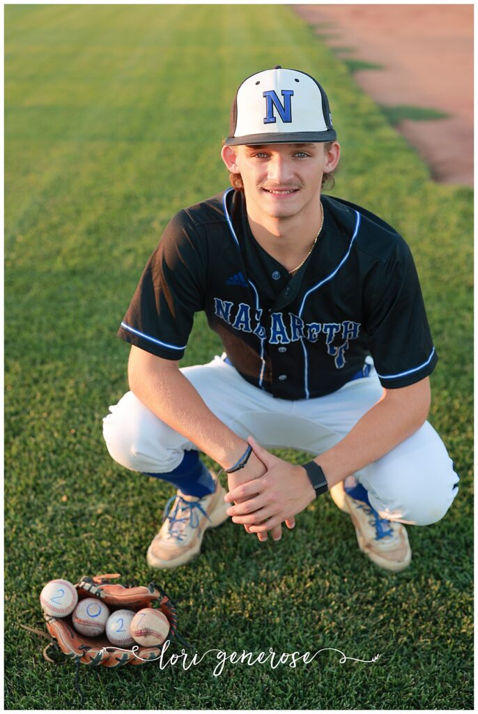 senior boy photoshoot of a Nazareth High School Baseball senior wearing his baseball uniform and squatting on the field with four baseballs with 2027 written on them laying in his open baseball glove at a baseball field in Nazareth, PA all taken by Lehigh Valley Senior photographer Lori Generose of LG Photography